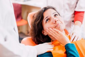 Woman holding face in pain in dentist’s chair.